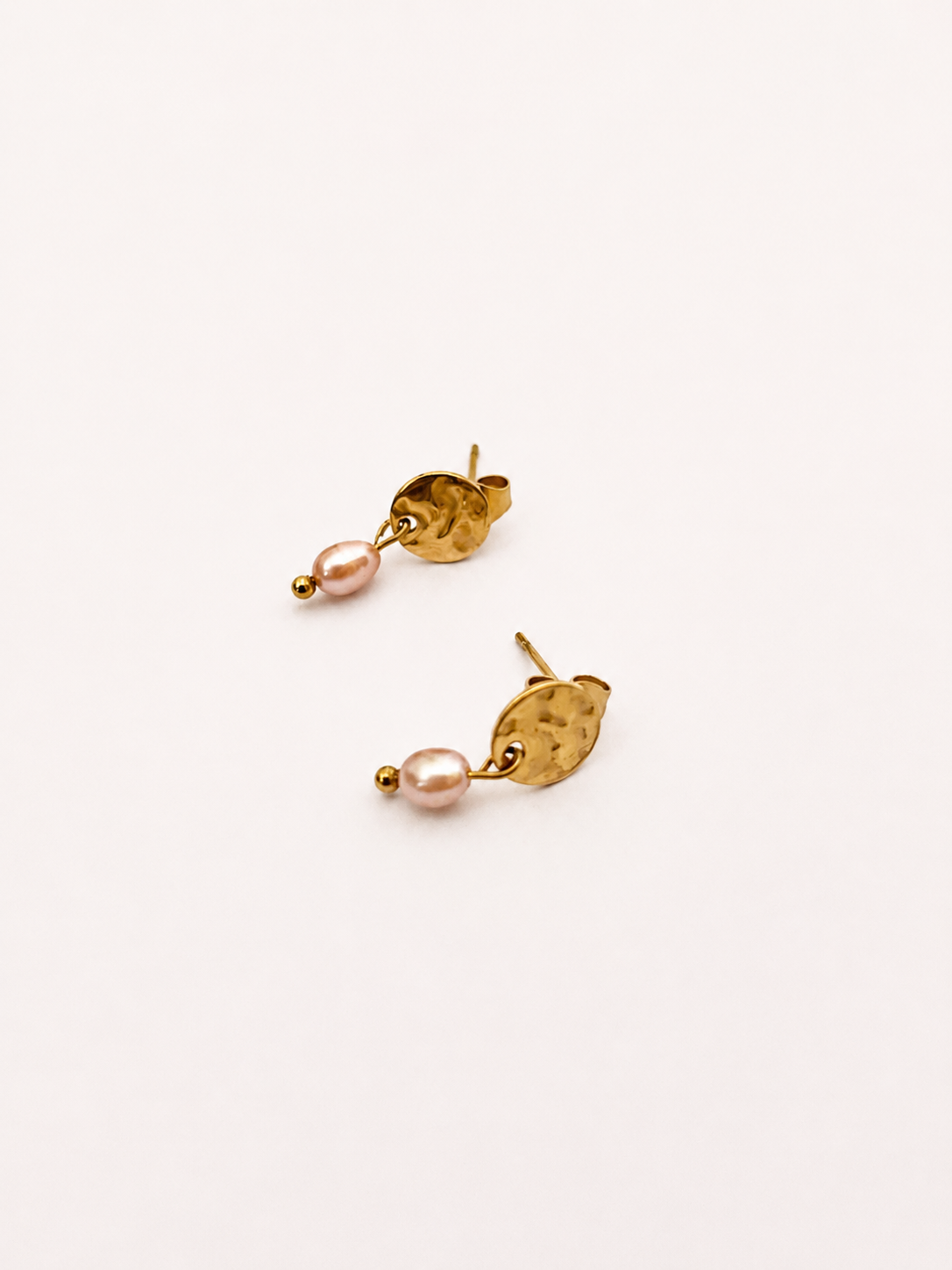 Angled view of gold stud earrings with 5 mm natural pink oval freshwater pearls.