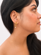 Woman wearing a minimalist gold stud earring with a natural pink oval freshwater pearl drop.