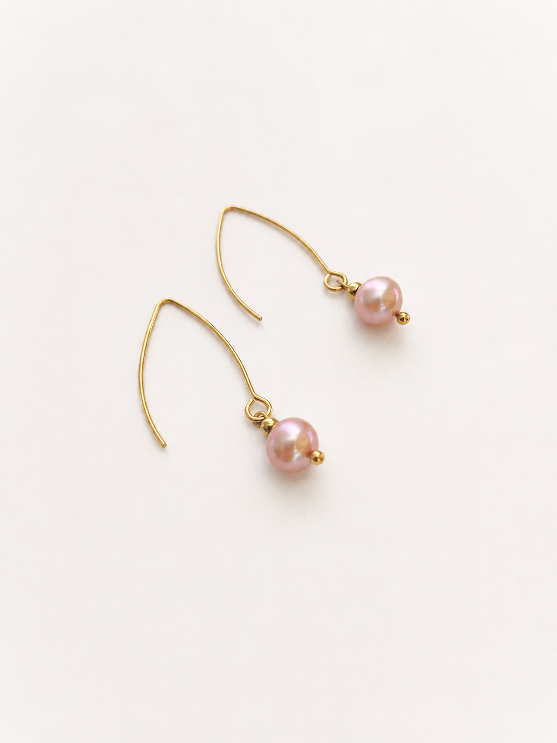 Angled view of gold drop earrings with 8 mm natural pink round freshwater pearls