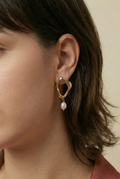Close-up detail of organic-shaped gold drop earrings featuring a small freshwater white oval pearl, worn by a model with a side profile view