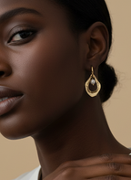 Close-up of a model wearing sculptural gold open-hoop earrings with a suspended white oval pearl. She is styled in a silver silk halter top and scarf, showcasing elegant minimalist bridal or evening jewelry