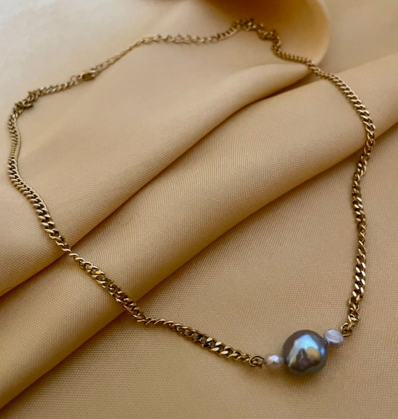 Close-up detail of an organic shaped grey pearl pendant on a gold curb chain, highlighting the iridescent nacre and handmade craftsmanship