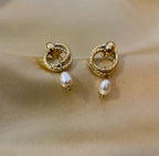 Women's textured gold interlocking hoop earrings with a genuine white pearl charm. High-resolution jewelry detail shot showing the clasp and finish.