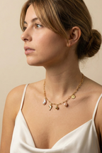 Elegant gold charm necklace with organic baroque pearls and sea-inspired pendants worn by a model with a messy bun; Parisian chic jewelry style