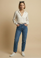 Editorial fashion portrait of a model wearing a mixed-metal gold chain necklace with grey and black baroque pearls. She is styled in a 'Parisian Chic' look with a white silk shirt and blue jeans, posing with hands in pockets against a neutral background