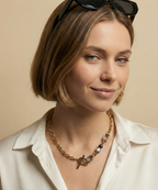 Editorial fashion portrait of a model wearing a mixed-metal gold chain necklace with grey and black baroque pearls.