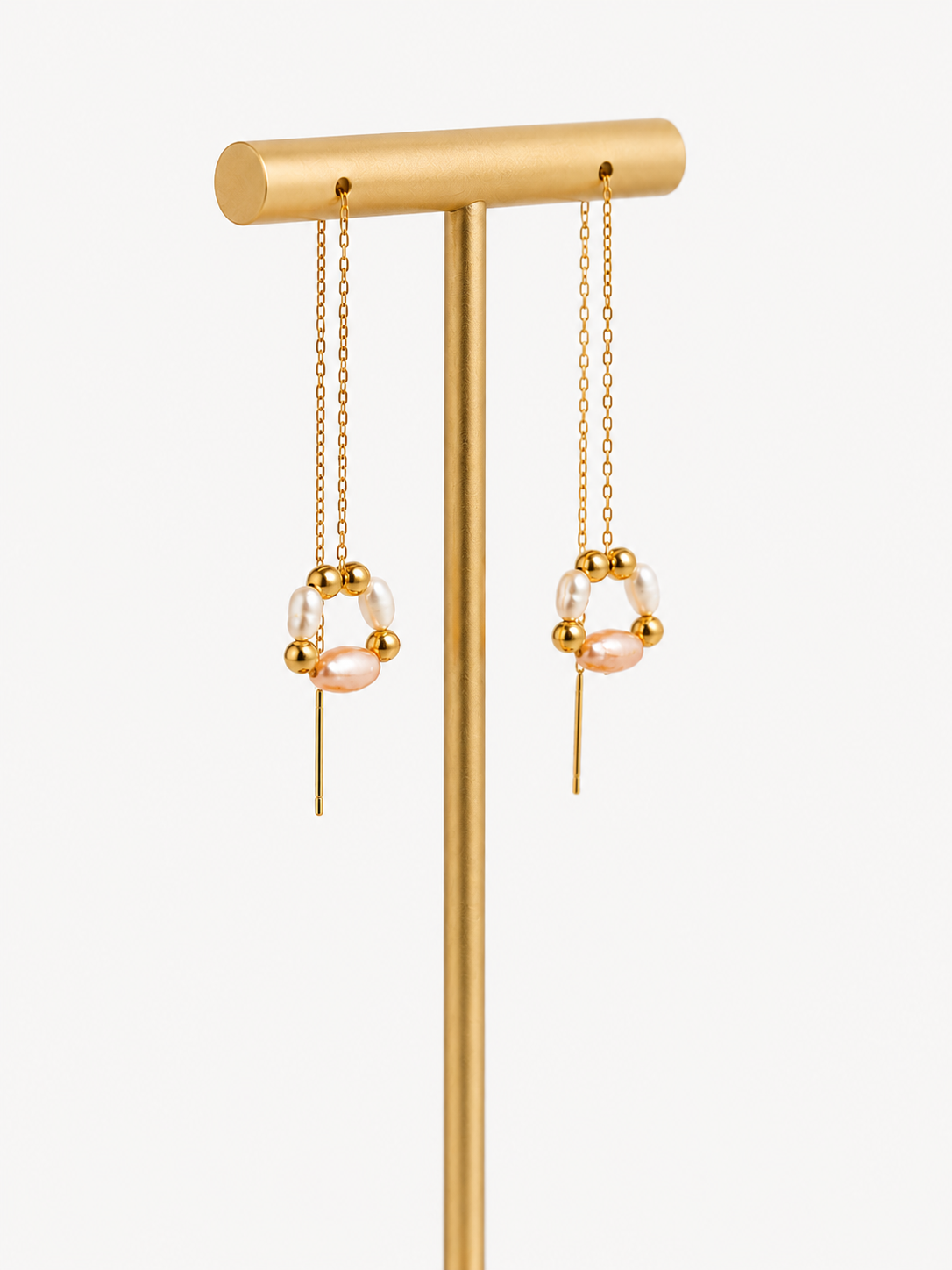 Pair of gold-plated threader drop earrings with white and blush freshwater pearls on a display stand