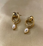 Women's textured gold interlocking hoop earrings with a genuine white pearl charm. High-resolution jewelry detail shot showing the clasp and finish.