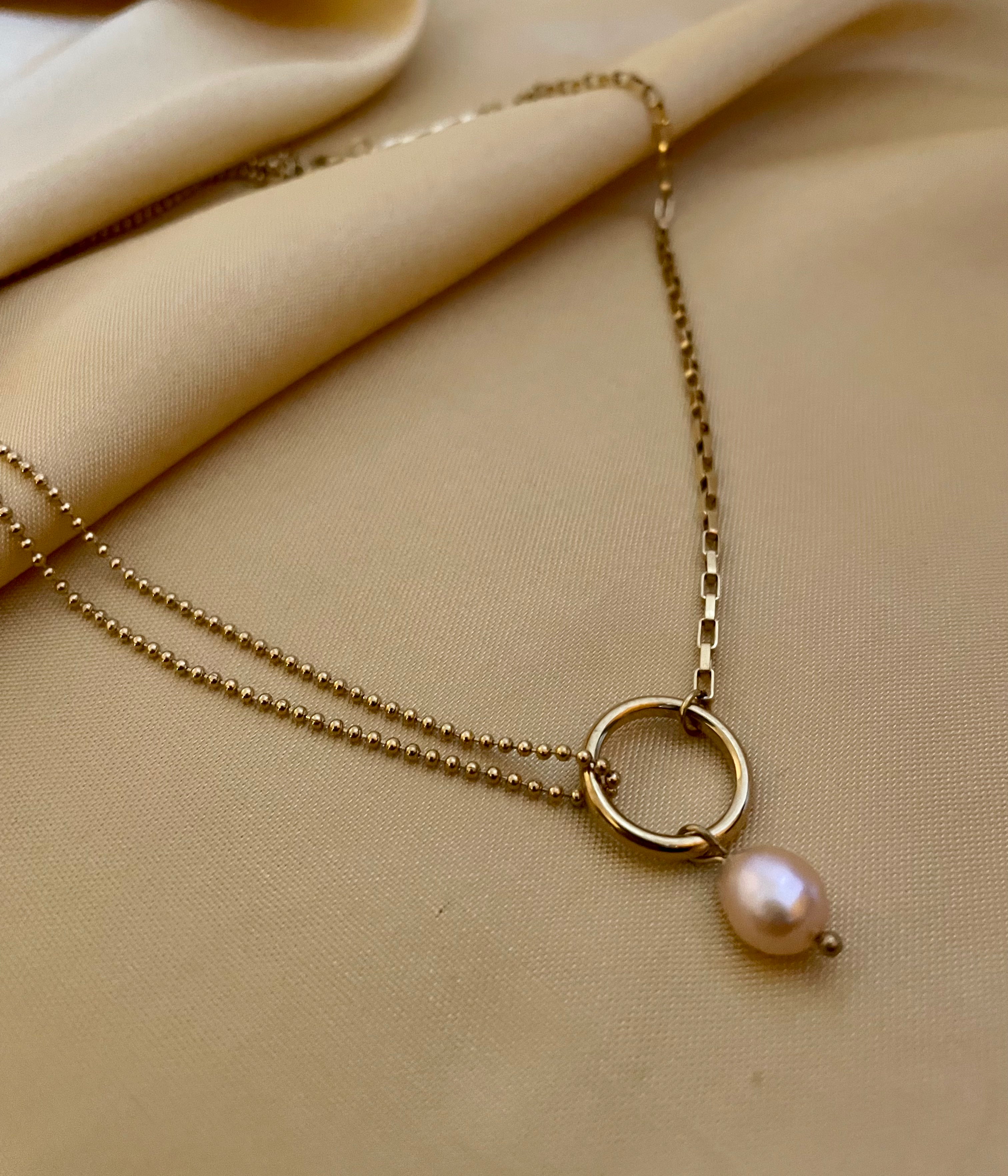 Gold necklace with a pearl pendant on a beige fabric background