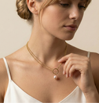 Woman wearing a gold necklace with a pearl pendant against a neutral background
