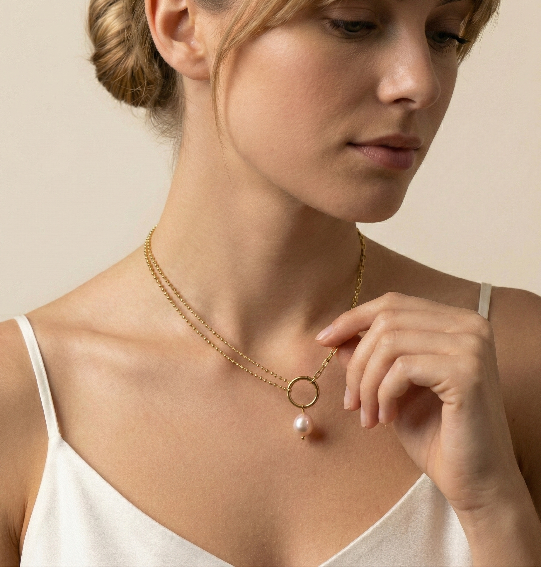 Woman wearing a gold necklace with a pearl pendant against a neutral background
