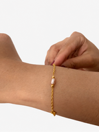 Close-up of a gold chain bracelet with a pink baroque pearl, gold beads and a small heart charm on the wrist