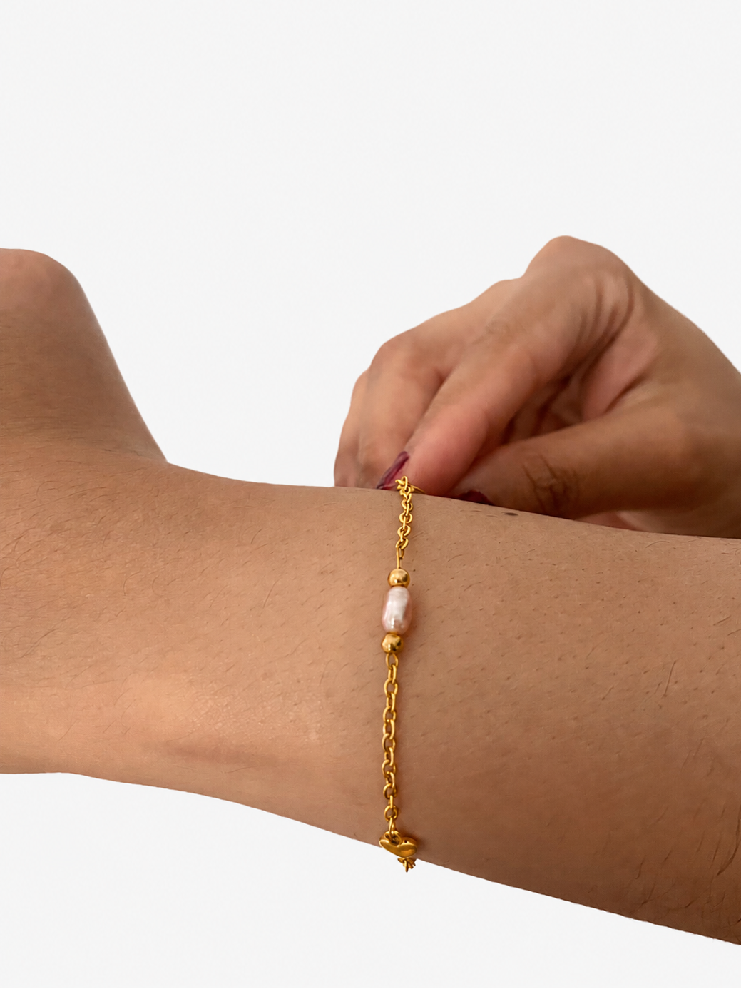 Close-up of a gold chain bracelet with a pink baroque pearl, gold beads and a small heart charm on the wrist