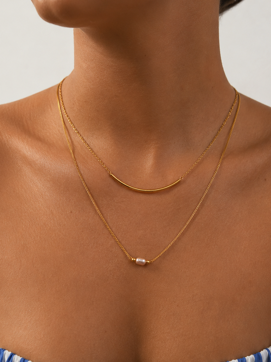 Woman wearing a layered gold Arc necklace with a 4 mm oval pink freshwater pearl and curved gold bar.