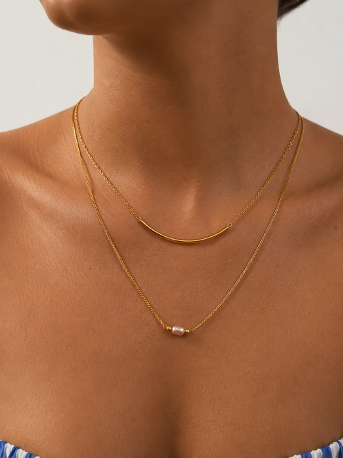 Woman wearing a layered gold Arc necklace with a 4 mm oval pink freshwater pearl and curved gold bar.
