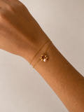 Close-up of a gold double-chain bracelet with a pink freshwater pearl pendant and polished gold beads
