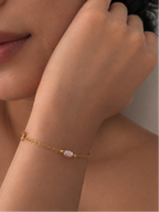 Woman wearing a delicate gold bracelet with a blush-pink pearl and polished gold beads