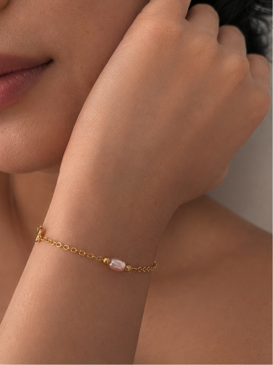 Woman wearing a delicate gold bracelet with a blush-pink pearl and polished gold beads