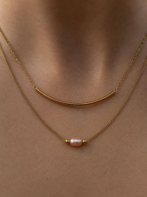 Close-up of a layered gold necklace with a 4 mm oval pink freshwater pearl and curved arc detail worn on the neck