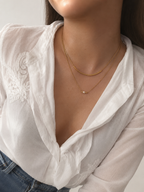 Lifestyle view of a layered gold necklace with an oval pink freshwater pearl and sculptural arc detail.