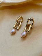 Close-up of gold U-link drop earrings featuring lustrous pink baroque pearls resting on a champagne silk background
