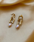 Pair of minimalist gold structural earrings with pink pearls, commercial jewelry photography on satin texture