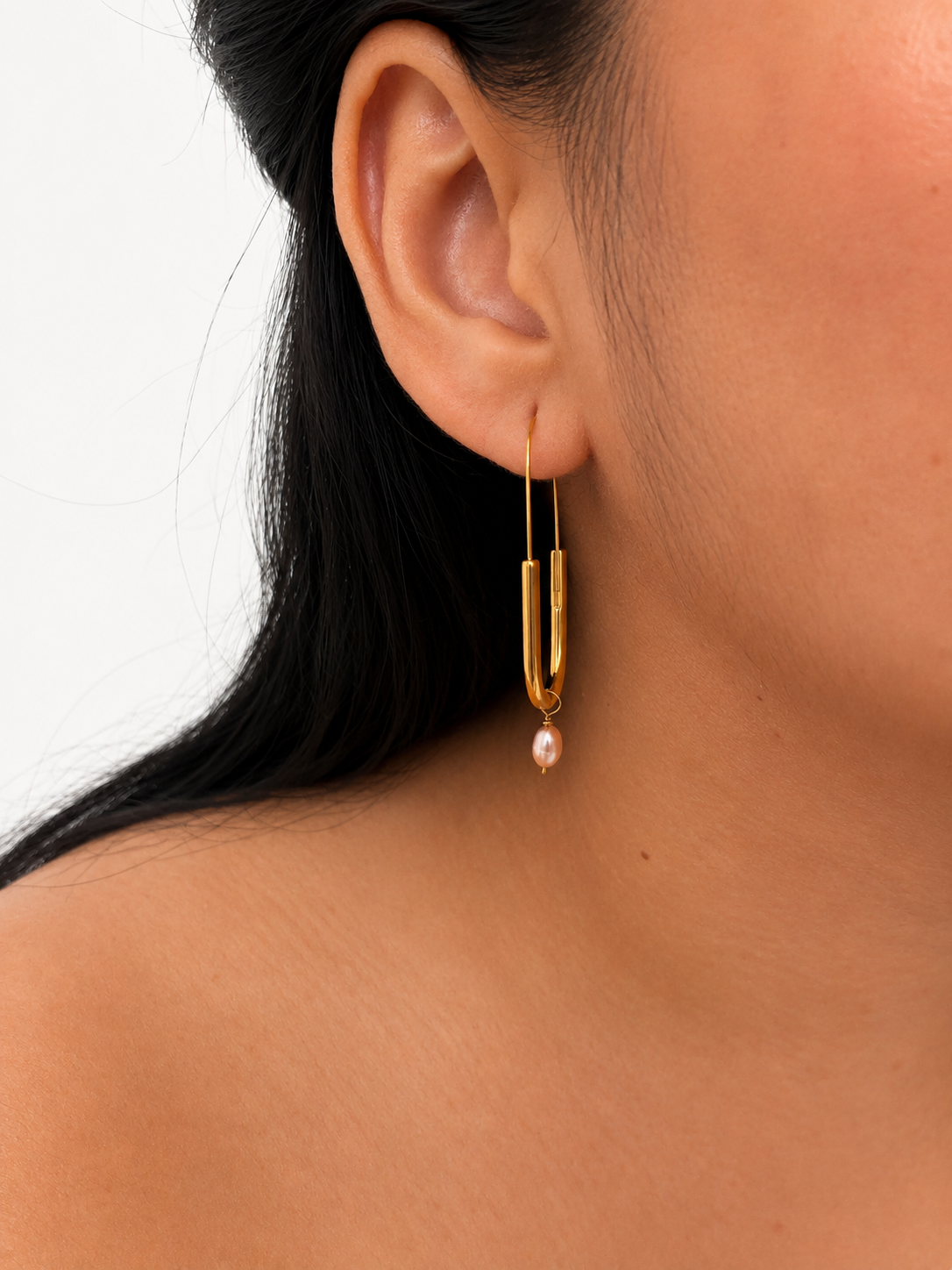 Close-up of a gold paperlink drop earring with an oval pink freshwater pearl worn on the ear.