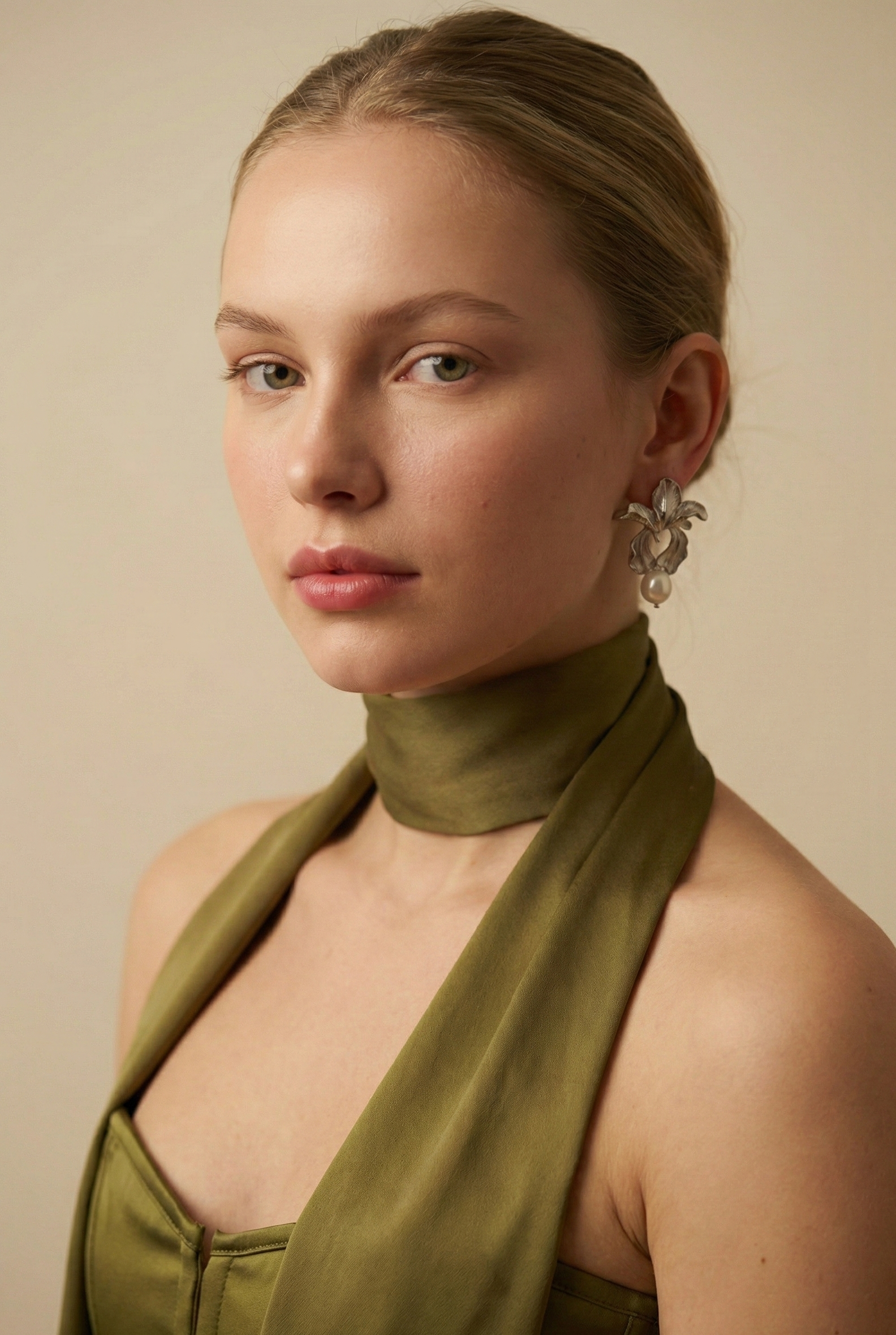 A model with a soft autumn complexion wearing silver botanical pearl earrings styled with an olive green silk scarf. The floral drop earrings frame the face elegantly