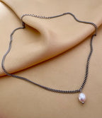 Close-up of a delicate silver curb chain necklace featuring a single white baroque pearl pendant with high luster
