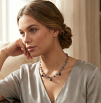 Model wearing a silver knotted link chain necklace featuring three round black pearl charms, styled with an olive green deep V-neck silk top