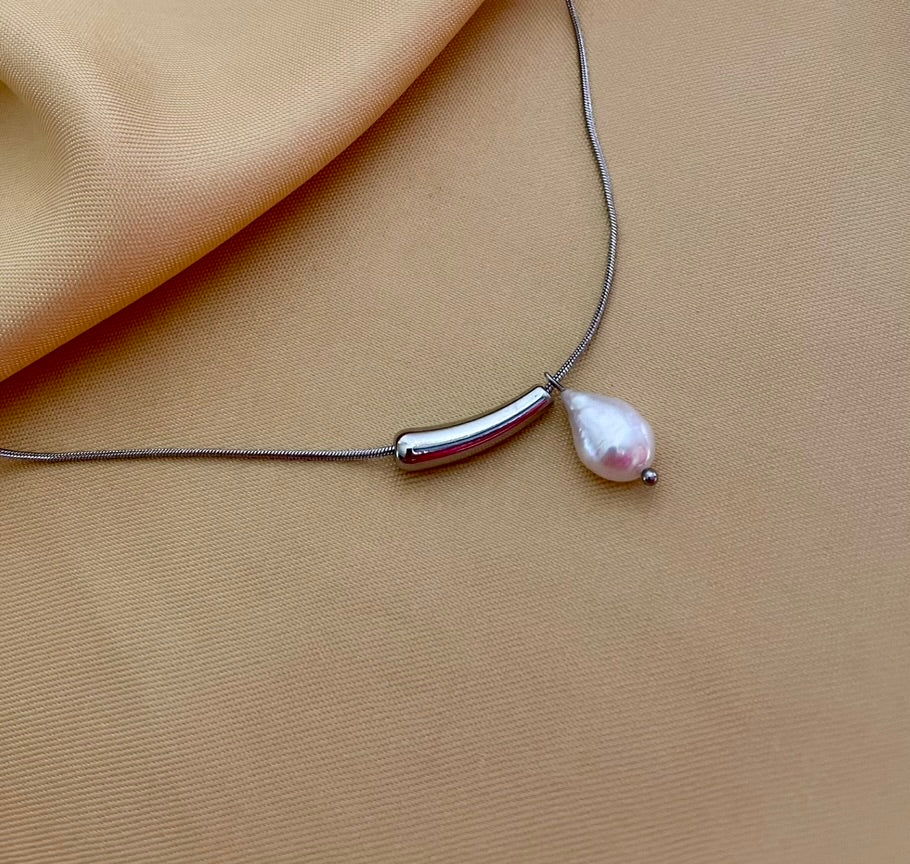 Close-up detail of a sterling silver snake chain necklace featuring a polished curved tube bar and a lustrous white keshi pearl drop