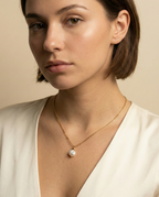 Detail shot of a woman wearing a simple gold necklace with a white pearl charm.