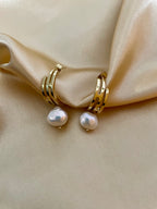 Gros plan sur des boucles d'oreilles pendantes en perles baroques blanches avec fermoir en or, portées par un mannequin