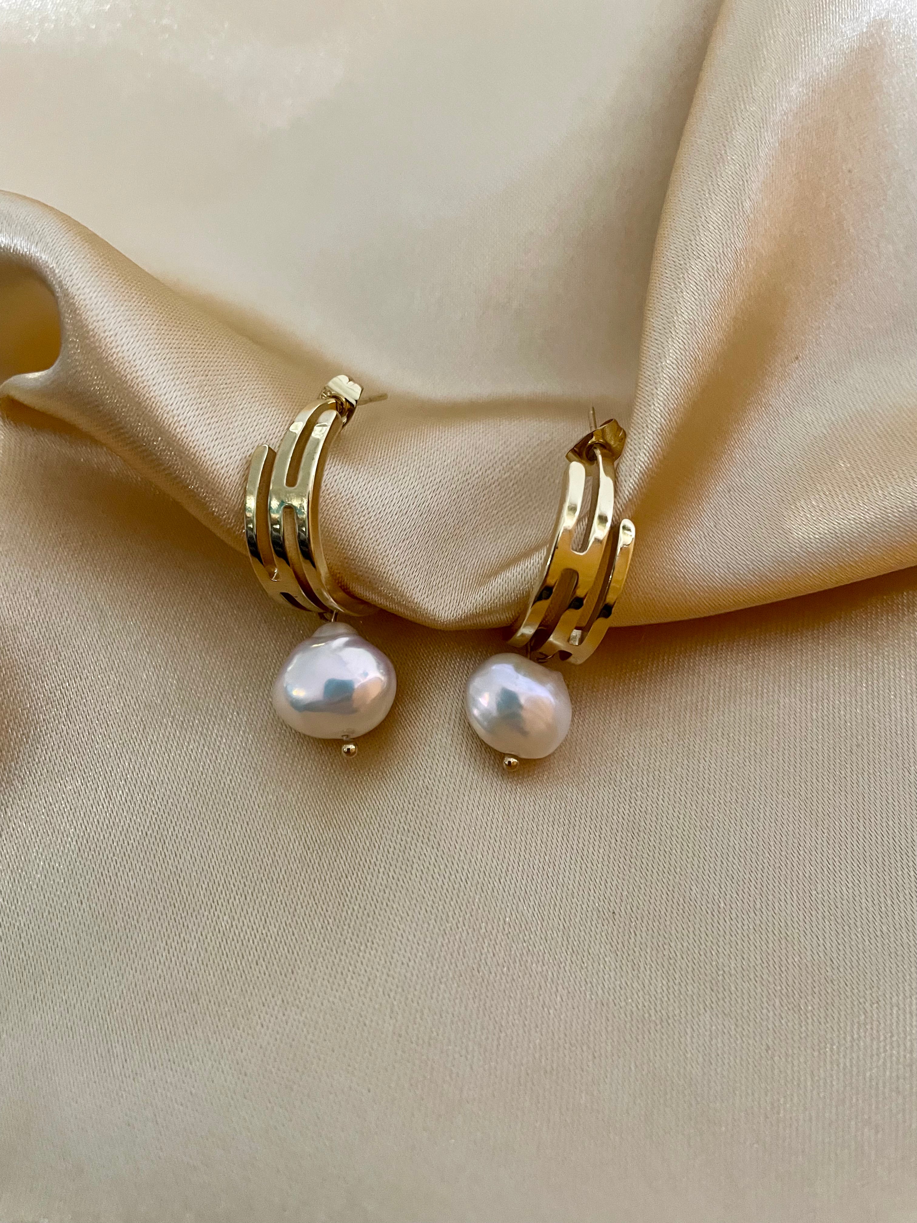 Gros plan sur des boucles d'oreilles pendantes en perles baroques blanches avec fermoir en or, portées par un mannequin