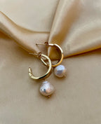 Gros plan sur des boucles d'oreilles pendantes en perles baroques blanches avec fermoir en or
