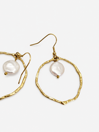 Angled close-up of textured gold hoop earrings with flat white freshwater coin pearls
