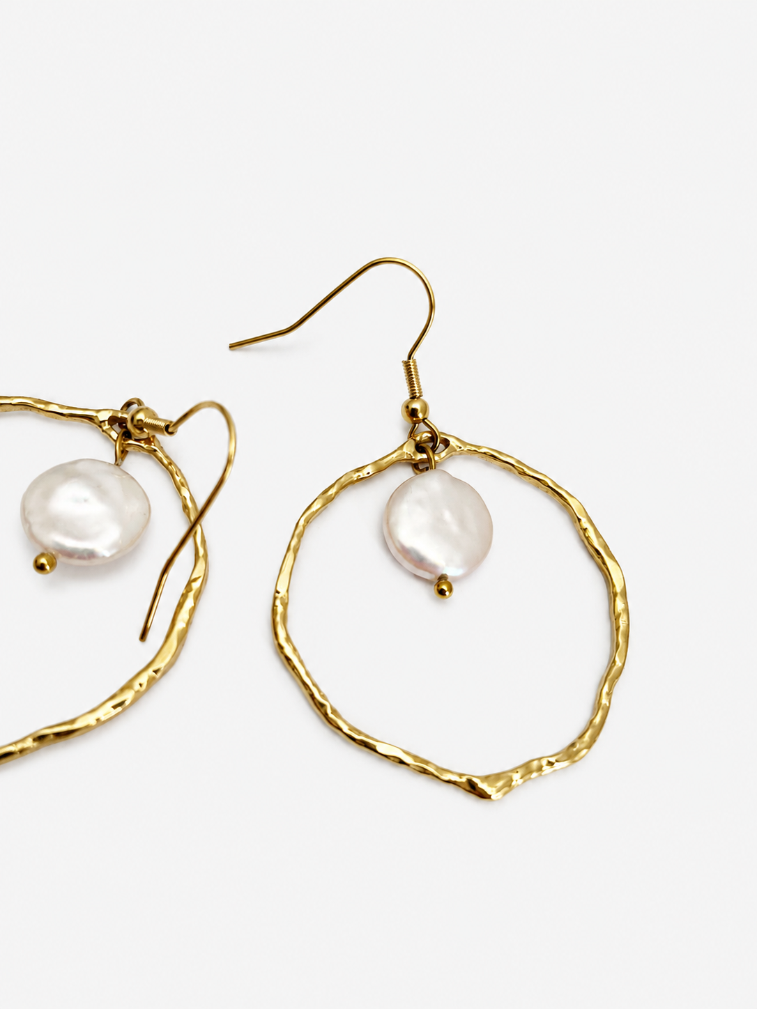 Angled close-up of textured gold hoop earrings with flat white freshwater coin pearls