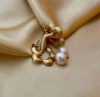 Close-up of textured gold huggie hoop earrings featuring a lustrous white pearl drop. The earrings have an organic, hammered gold finish