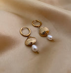 Close-up detail of gold scallop shell earrings featuring a lustrous white pearl drop. The earrings are worn by a model to show scale, highlighting the textured gold finish and elegant dangle design perfect for beach weddings or summer luxury