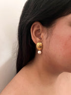 Woman wearing a textured gold drop earring with a white baroque freshwater pearl