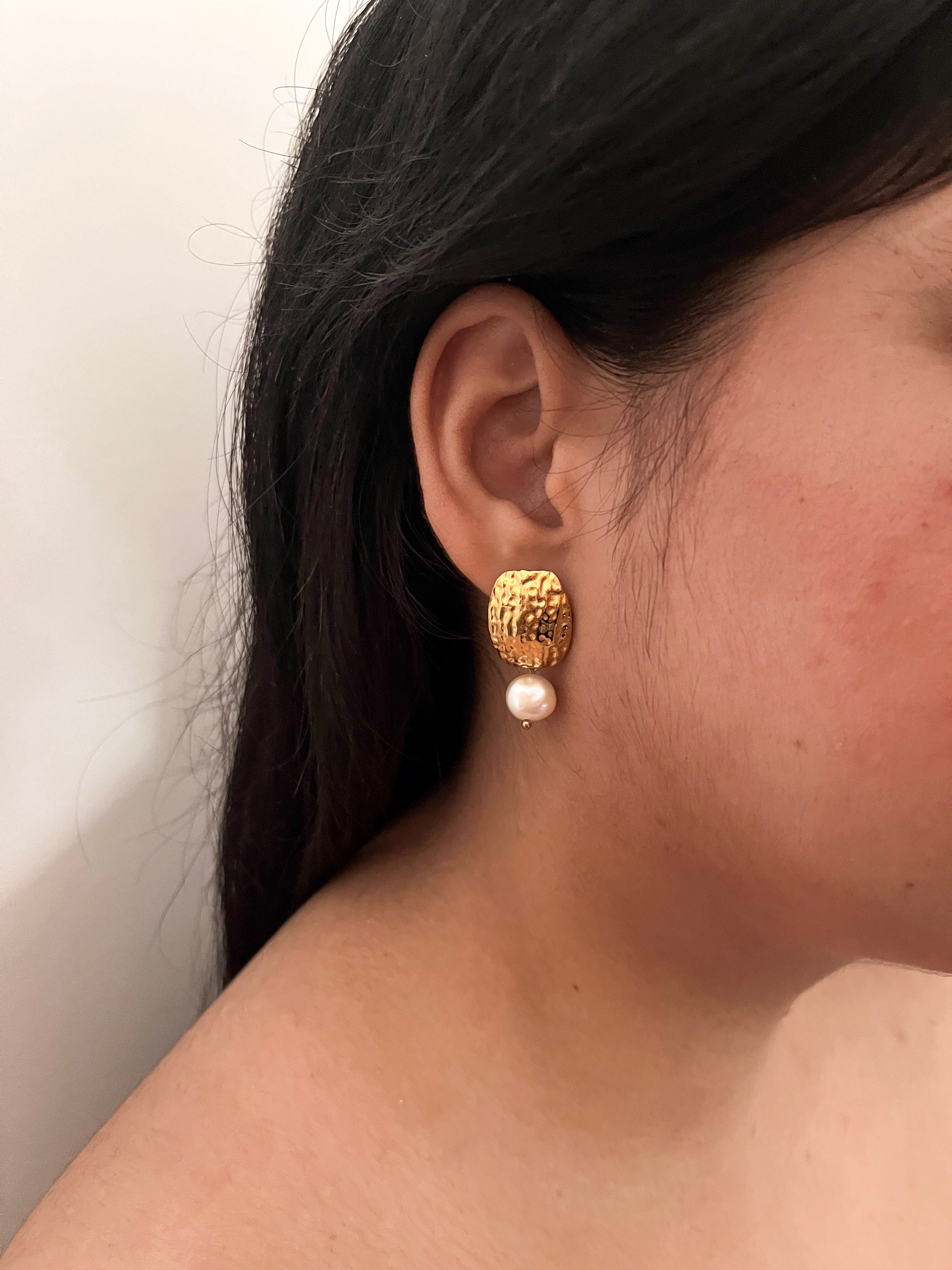 Woman wearing a textured gold drop earring with a white baroque freshwater pearl