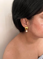 Side view of a textured gold earring with a white freshwater baroque pearl drop worn on the ear.