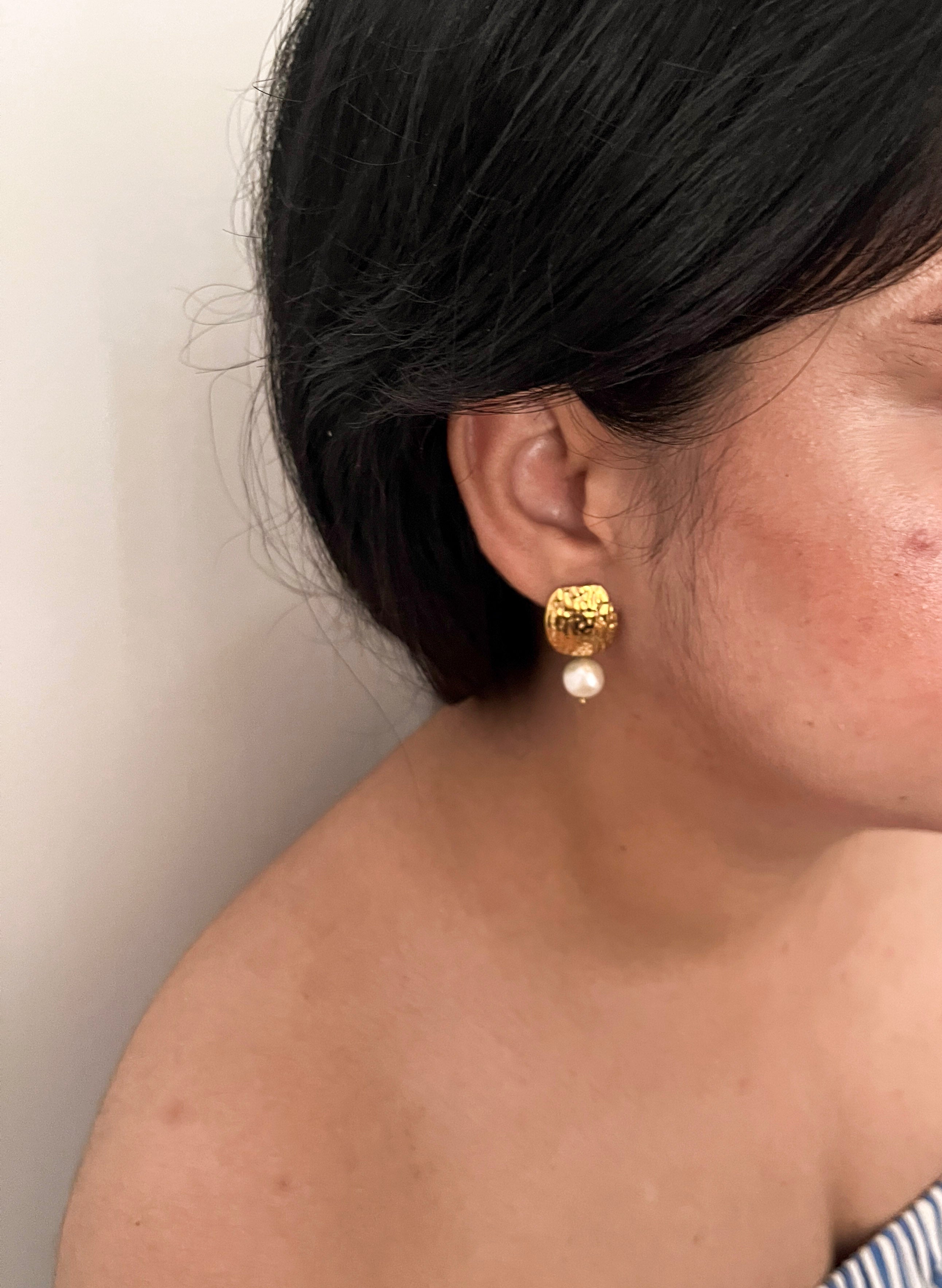 Side view of a textured gold earring with a white freshwater baroque pearl drop worn on the ear.