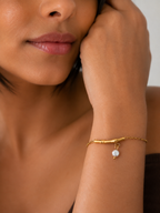 Close portrait of a woman wearing a gold twig bar bracelet with a pale grey freshwater pearl drop