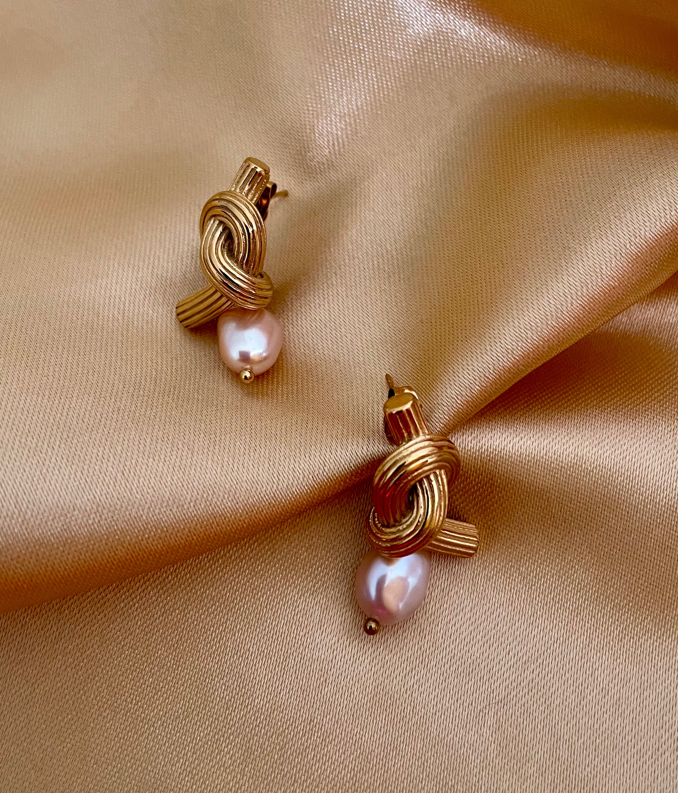 Pair of gold-knot earrings with pearls on a beige fabric background