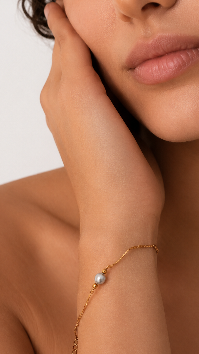 Woman wearing a delicate gold bracelet with a grey freshwater pearl and polished gold beads