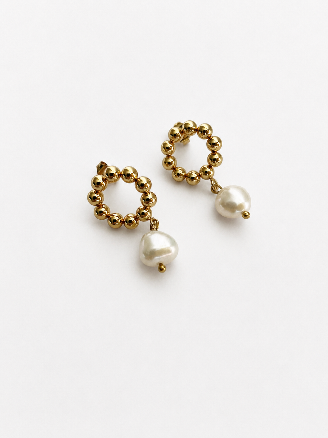 Angled view of gold beaded drop earrings with organic white baroque freshwater pearl drops