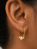 Close-up of a small gold creole earring with clustered white baroque freshwater pearls worn on the ear