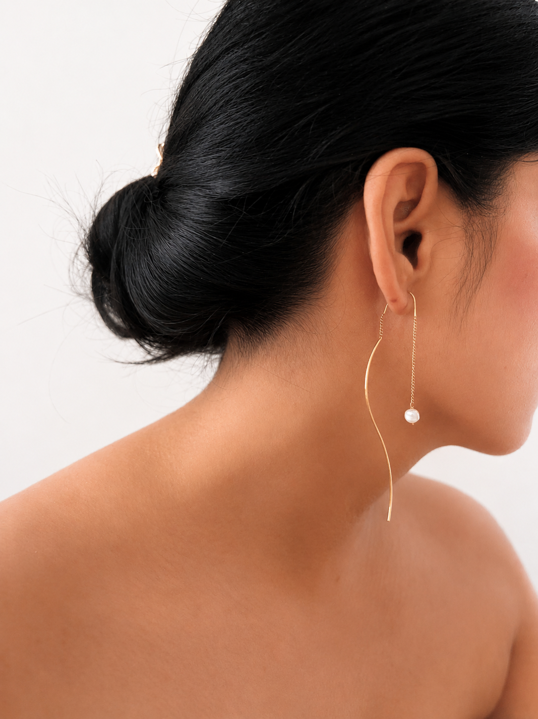 Woman wearing a curved gold drop earring with a 6 mm white baroque freshwater pearl.