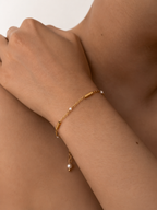 Close-up of a delicate gold bracelet with 2 mm white baroque freshwater pearls worn on the wrist.